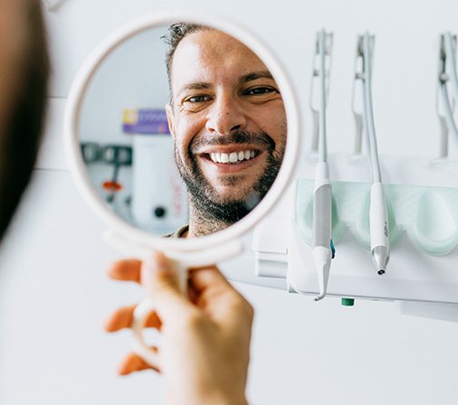 Man smiling at reflection in handheld mirror